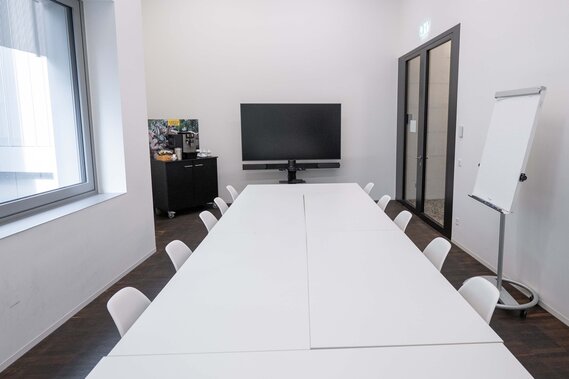 Ein Sitzungsraum mit Betonwänden und einem Tisch mit Stühlen rundherum.