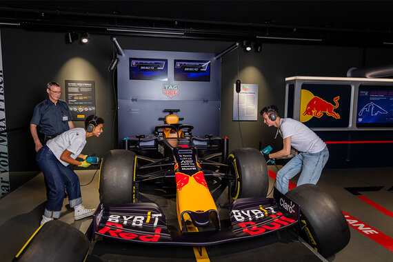 Zwei Personen stellen spielerisch einen Reifenwechsel an einem Red Bull Formel-1-Auto nach.