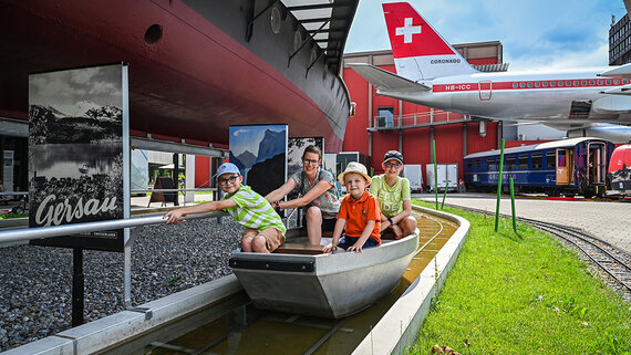 Kinder spielen in einem kleinen Boot, dass ein kleiner Fluss eine Familie um ein riesiges Schiffsmodell herumführt.