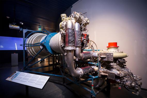  Ein Düsentriebwerk mit komplizierten Metallkomponenten, Rohrleitungen und Steuersystemen, präsentiert in einem modernen Ausstellungsraum.