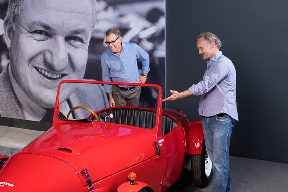 Zwei Herren stehen vor einem roten Monteverdi-Auto und diskutieren.