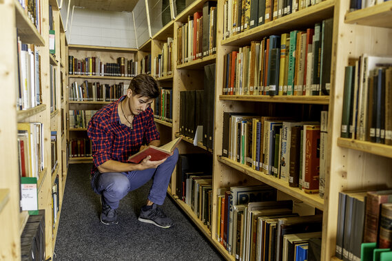 Eine Person liest ein Buch zwischen Bücherregalen in der Bibliothek des Dokuzentrums im Verkehrshaus.
