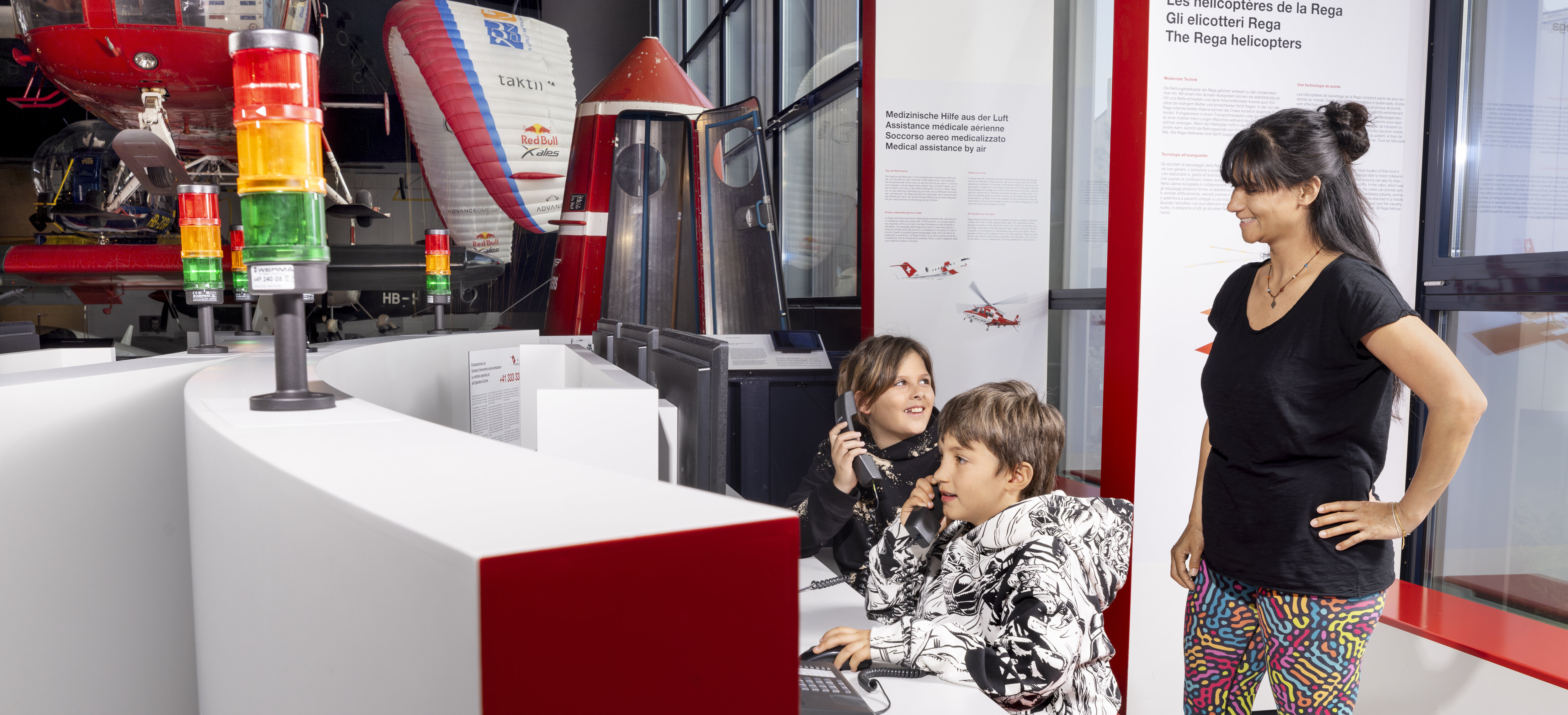 Zwei Kinder halten sich Telefonhörer ans Ohr, die Mutter schaut zu.