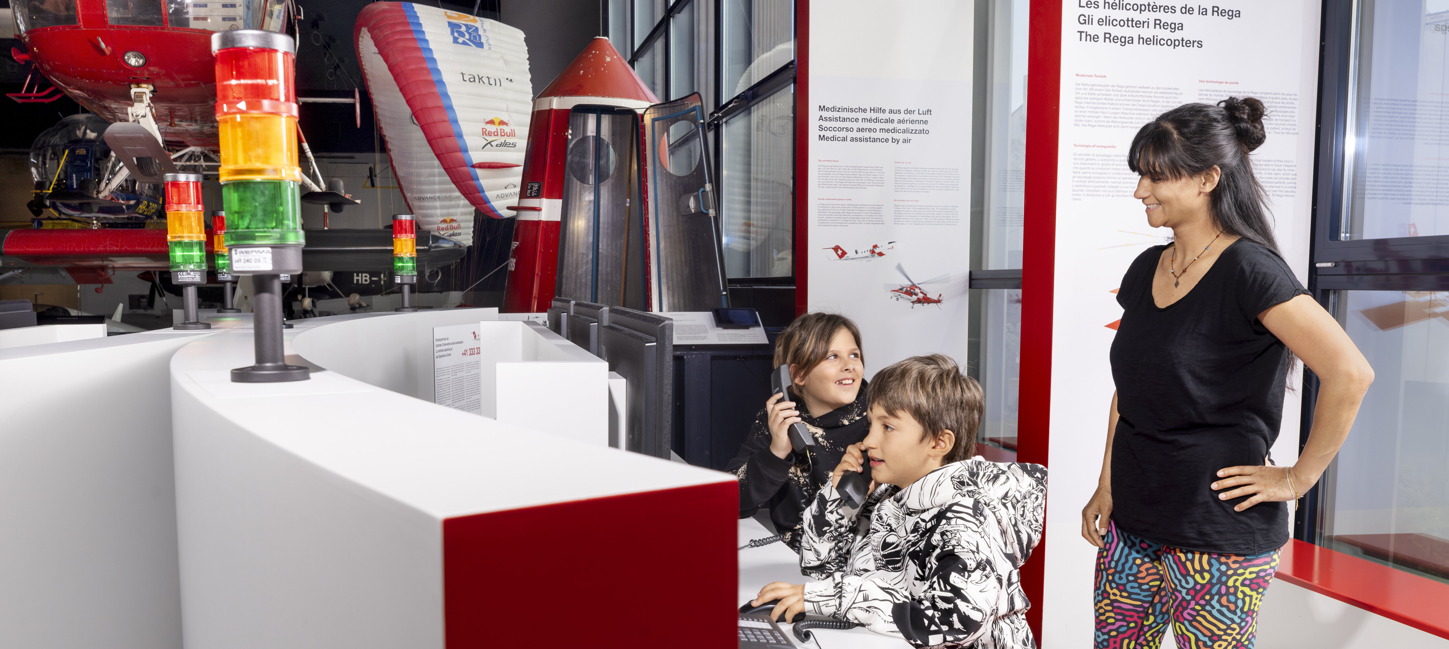 Zwei Kinder halten sich Telefonhörer ans Ohr, die Mutter schaut zu.
