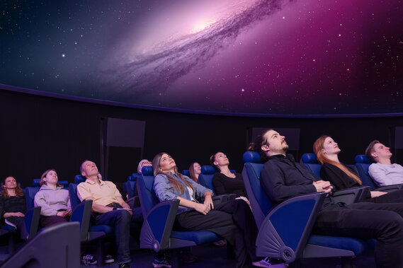 Personen sitzen in Lehnstühlen im Verkehrshaus Planetarium und schauen das Weltall an, das in der Kuppel projiziert wird. 