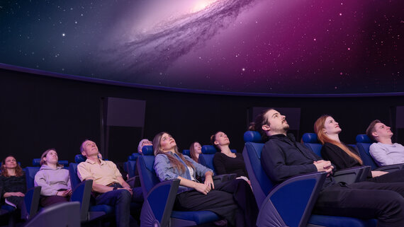 Personen sitzen in Lehnstühlen im Verkehrshaus Planetarium und schauen das Weltall an, das in der Kuppel projiziert wird. 