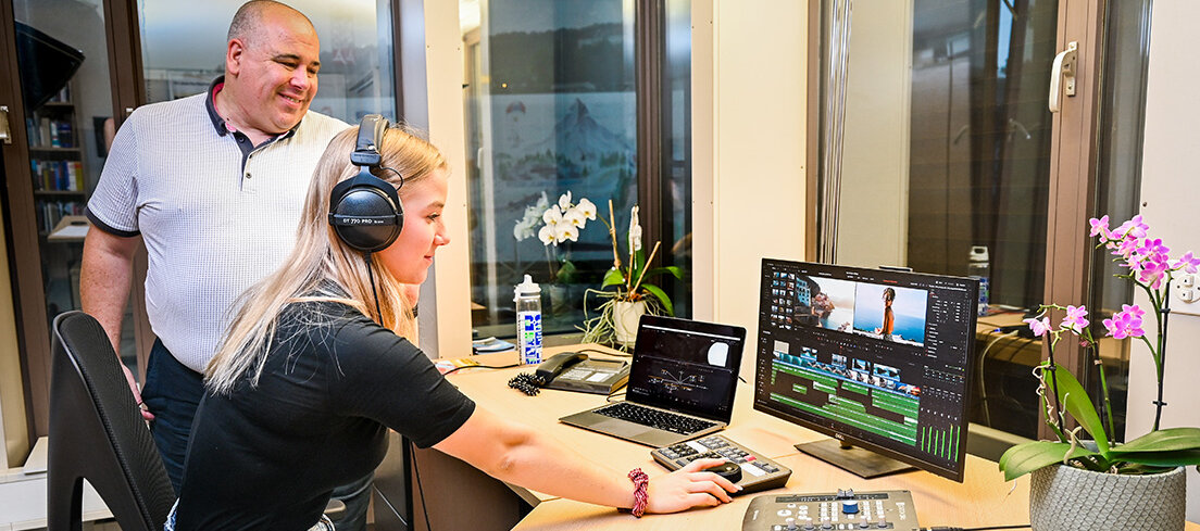 Ein Lehrling übt den Schnitt eines Werbevideos, während der Ausbilder die Arbeit kontrolliert.