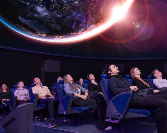 Personen sitzen in Lehnstühlen im Verkehrshaus Planetarium und schauen das Weltall an, das in der Kuppel projiziert wird. 