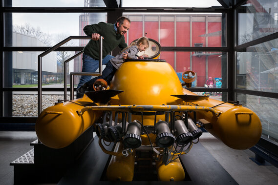 Ein Vater schaut mit seinem Kind in ein gelbes Uboot, welches in der Ausstellung des Verkehrshauses steht.