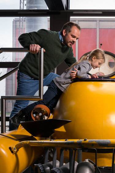 Ein Vater schaut mit seinem Kind in ein gelbes Uboot, welches in der Ausstellung des Verkehrshauses steht.