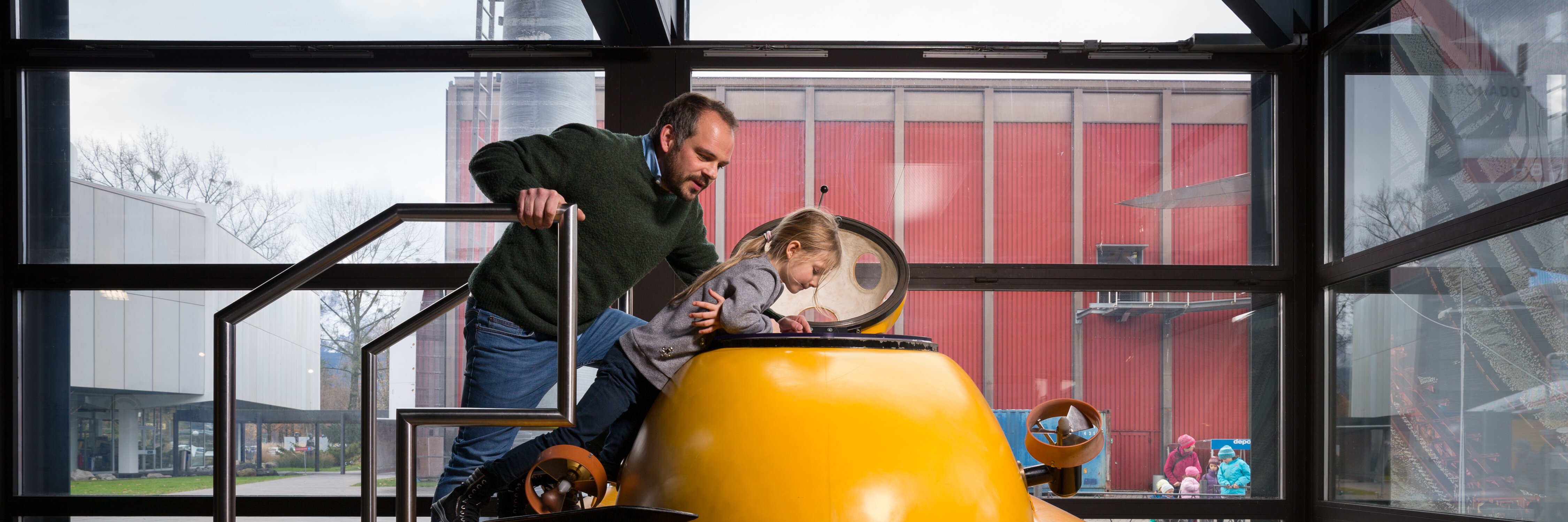 Ein Vater schaut mit seinem Kind in ein gelbes Uboot, welches in der Ausstellung des Verkehrshauses steht.