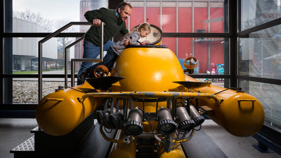 Ein Vater schaut mit seinem Kind in ein gelbes Uboot, welches in der Ausstellung des Verkehrshauses steht.
