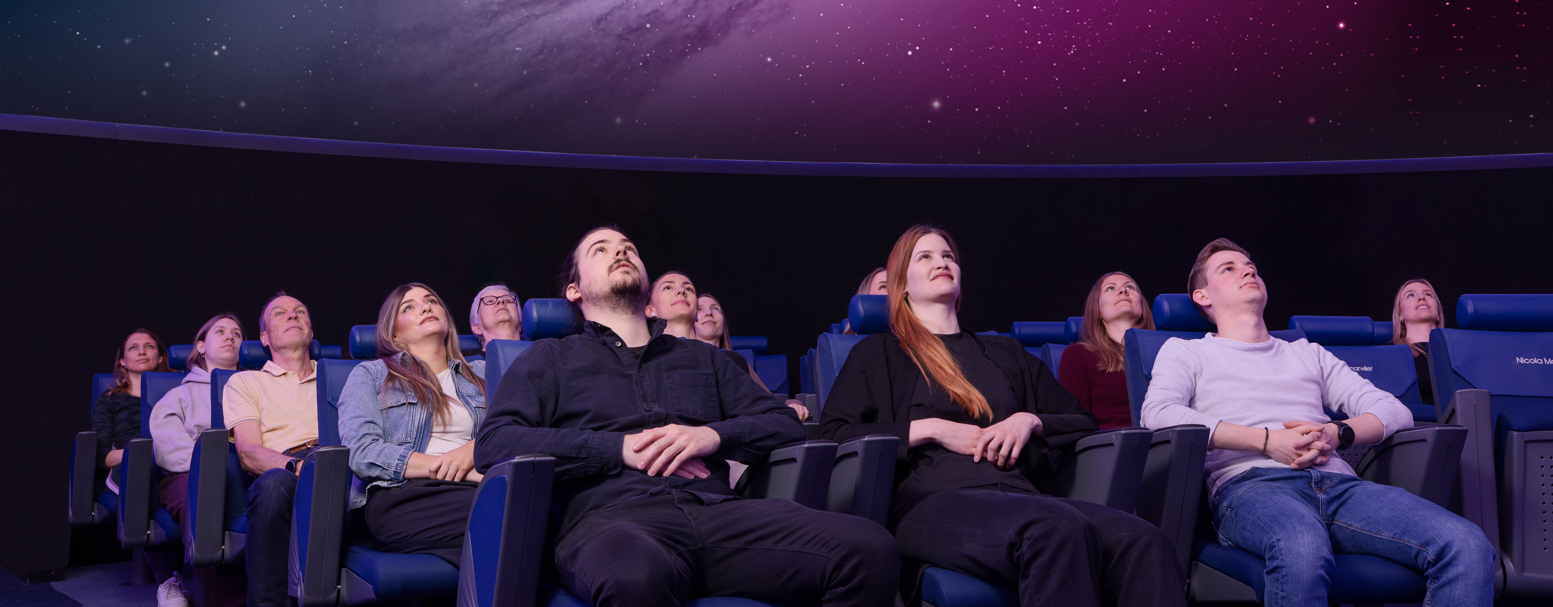 Personen sitzen in Lehnstühlen im Verkehrshaus Planetarium und schauen das Weltall an, das in der Kuppel projiziert wird.
