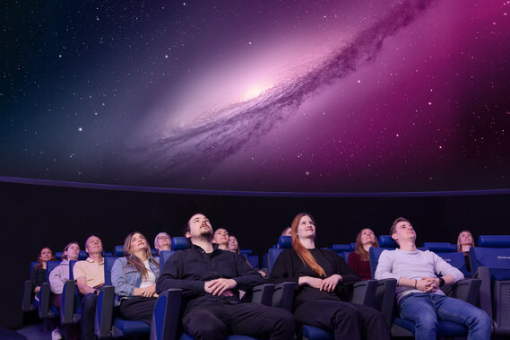 Personen sitzen in Lehnstühlen im Verkehrshaus Planetarium und schauen das Weltall an, das in der Kuppel projiziert wird. 