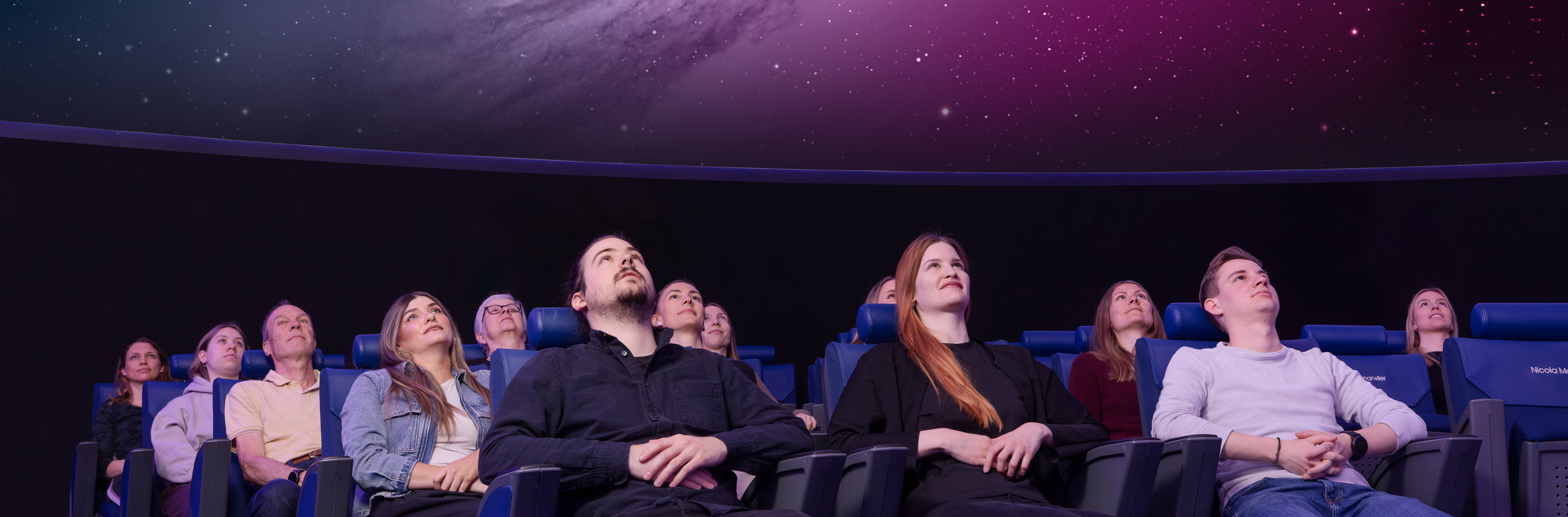 Personen sitzen in Lehnstühlen im Verkehrshaus Planetarium und schauen das Weltall an, das in der Kuppel projiziert wird. 