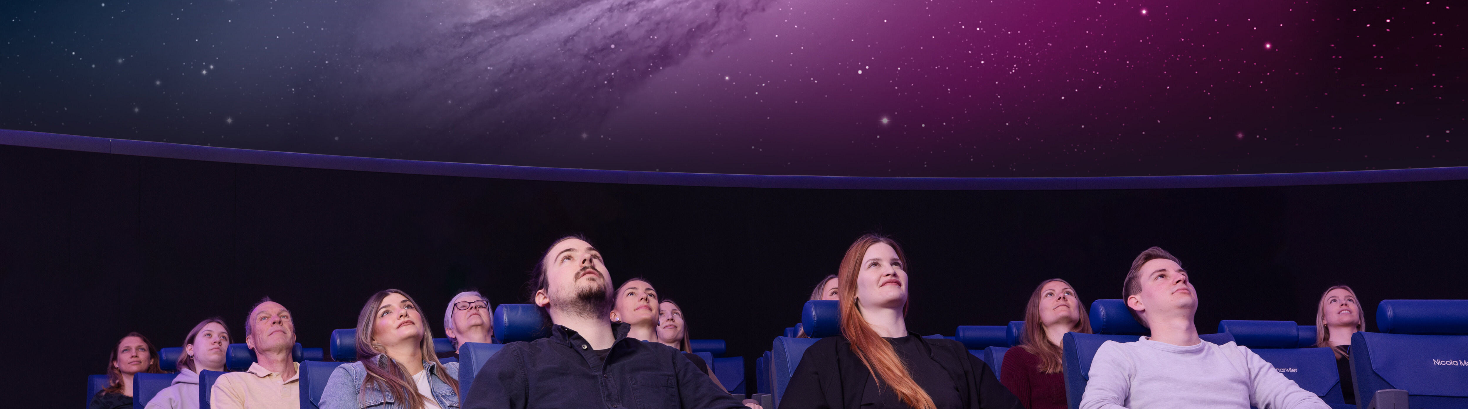 Personen sitzen in Lehnstühlen im Verkehrshaus Planetarium und schauen das Weltall an, das in der Kuppel projiziert wird.