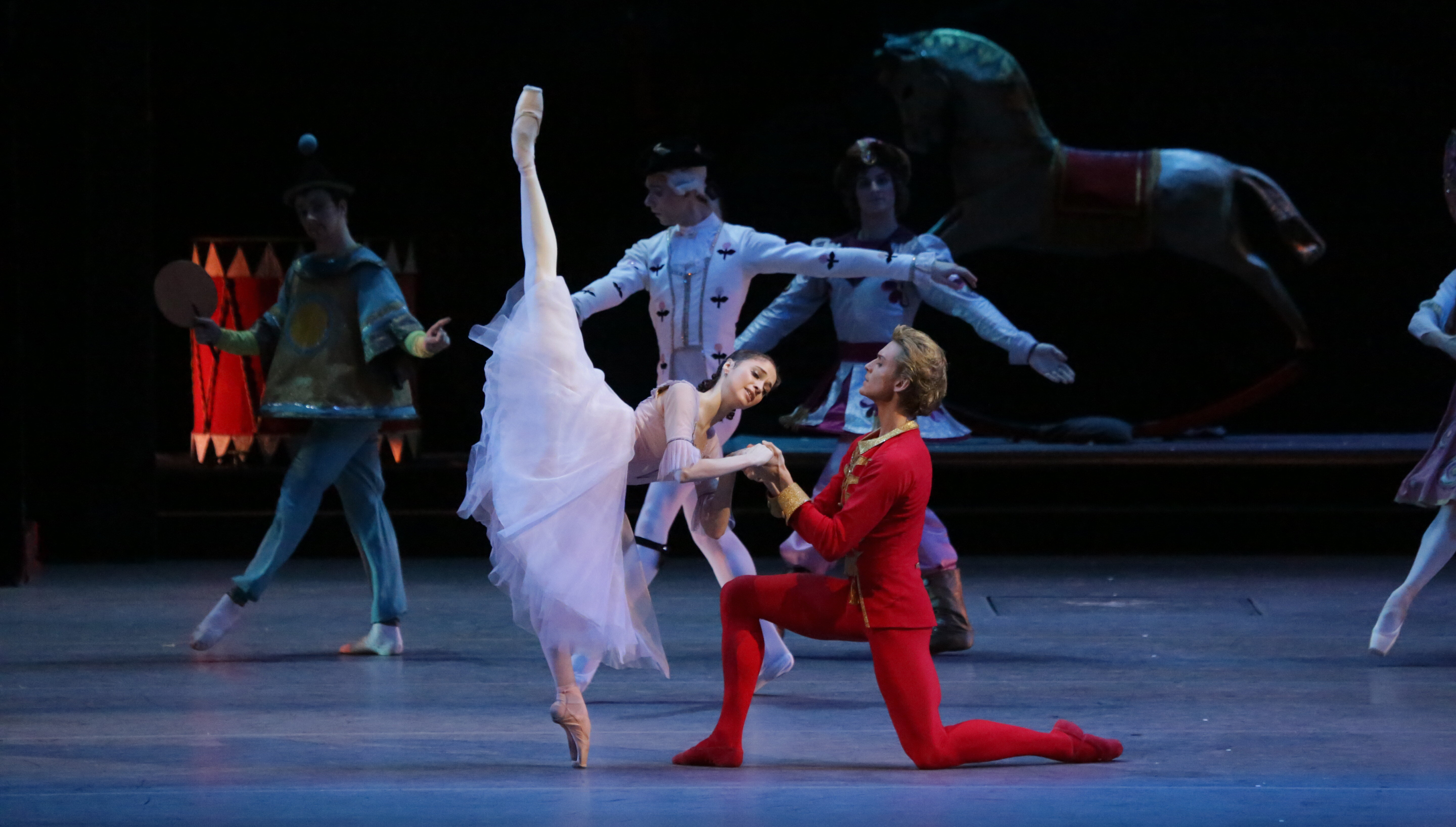 Eine Balletttänzerin streckt ihr Bein längs in die Luft und ein männlicher Balletttänzer kniet daneben.