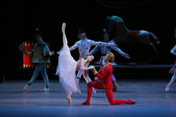 Eine Balletttänzerin streckt ihr Bein längs in die Luft und ein männlicher Balletttänzer kniet daneben.