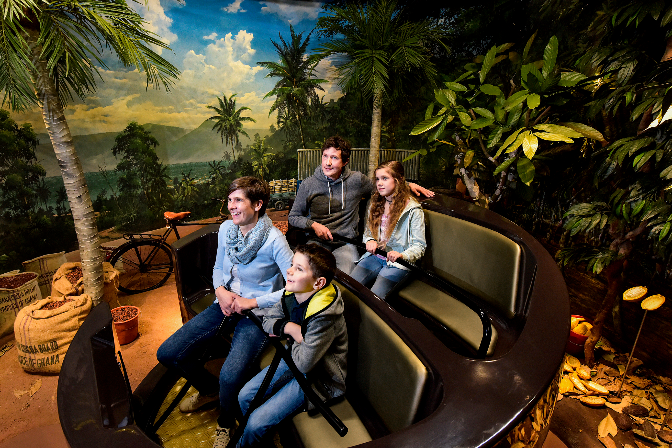 Eine vierköpfige Familie in einem Achterbahn-Wagen, rundherum ist eine Djungle-Welt zu sehen.