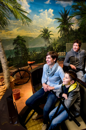 Eine vierköpfige Familie in einem Achterbahn-Wagen, rundherum ist eine Djungle-Welt zu sehen.