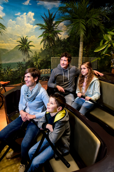 Eine vierköpfige Familie in einem Achterbahn-Wagen, rundherum ist eine Djungle-Welt zu sehen.