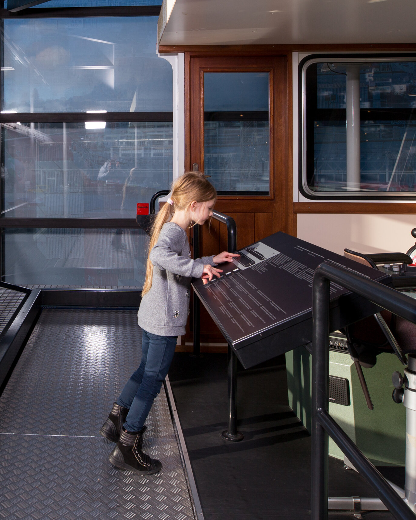 Ein Mädchen steht in einem Cockpit eines Schiffs in der Schifffahrtshalle des Verkehrshaus der Schweiz.