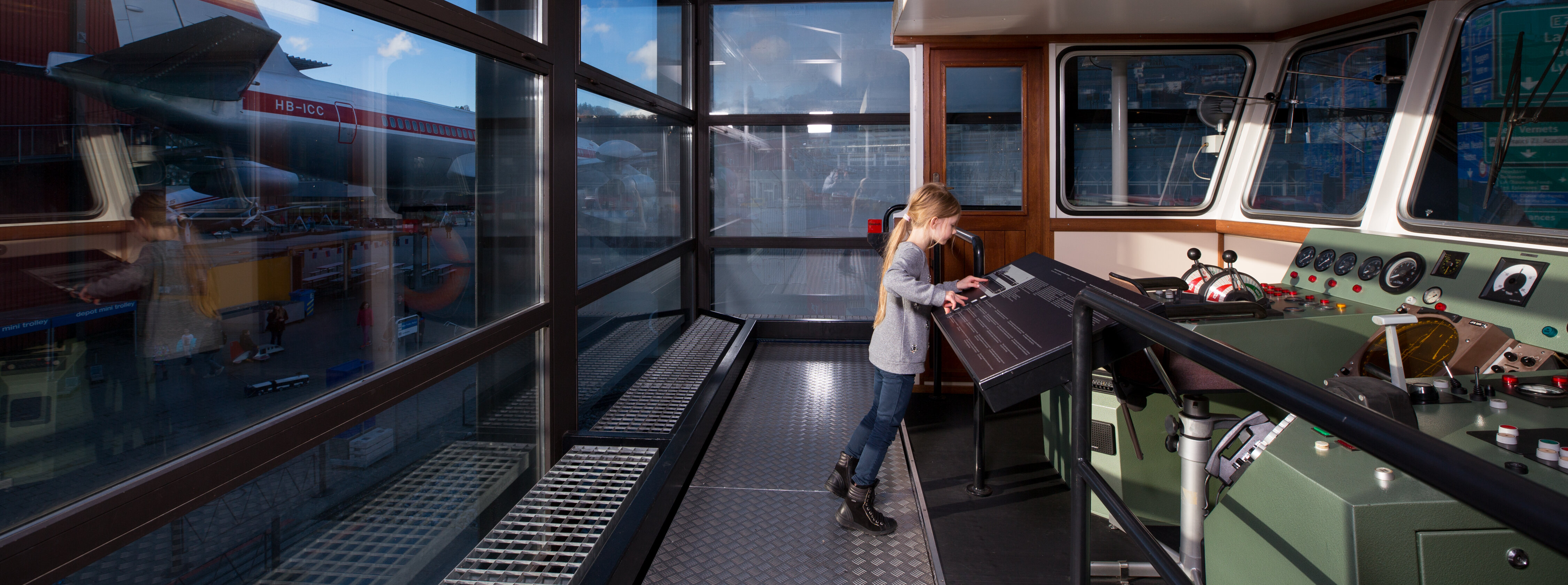 Ein Mädchen steht in einem Cockpit eines Schiffs in der Schifffahrtshalle des Verkehrshaus der Schweiz.