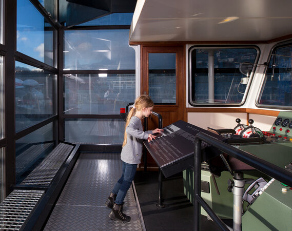 Ein Mädchen steht in einem Cockpit eines Schiffs in der Schifffahrtshalle des Verkehrshaus der Schweiz.