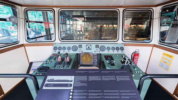 Ansicht eines alten Schiffskontrollraums mit verschiedenen Anzeigen, Hebeln und einem Radarbildschirm, der die nautischen Navigationsgeräte zeigt.