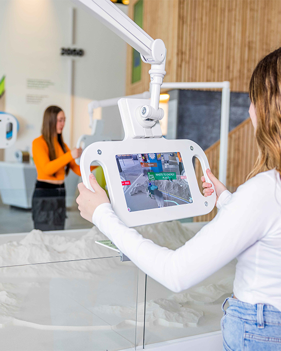 Ein Mädchen interagiert mit einem Touchscreen-Tablet und erkundet ein 3D-Geländemodell im Verkehrsmuseum..