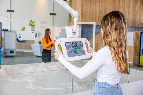 Ein Mädchen interagiert mit einem Touchscreen-Tablet und erkundet ein 3D-Geländemodell im Verkehrsmuseum..