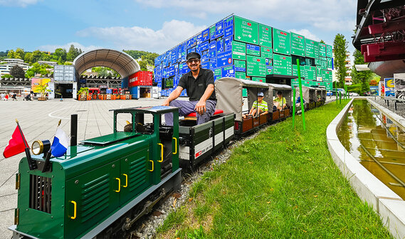 Eine grüne Miniatur-Eisenbahn fährt auf einer Schiene in einem Außenbereich des Verkehrshauses der Schweiz.