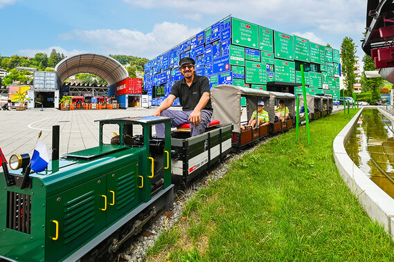 Eine grüne Miniatur-Eisenbahn fährt auf einer Schiene in einem Außenbereich des Verkehrshauses der Schweiz.