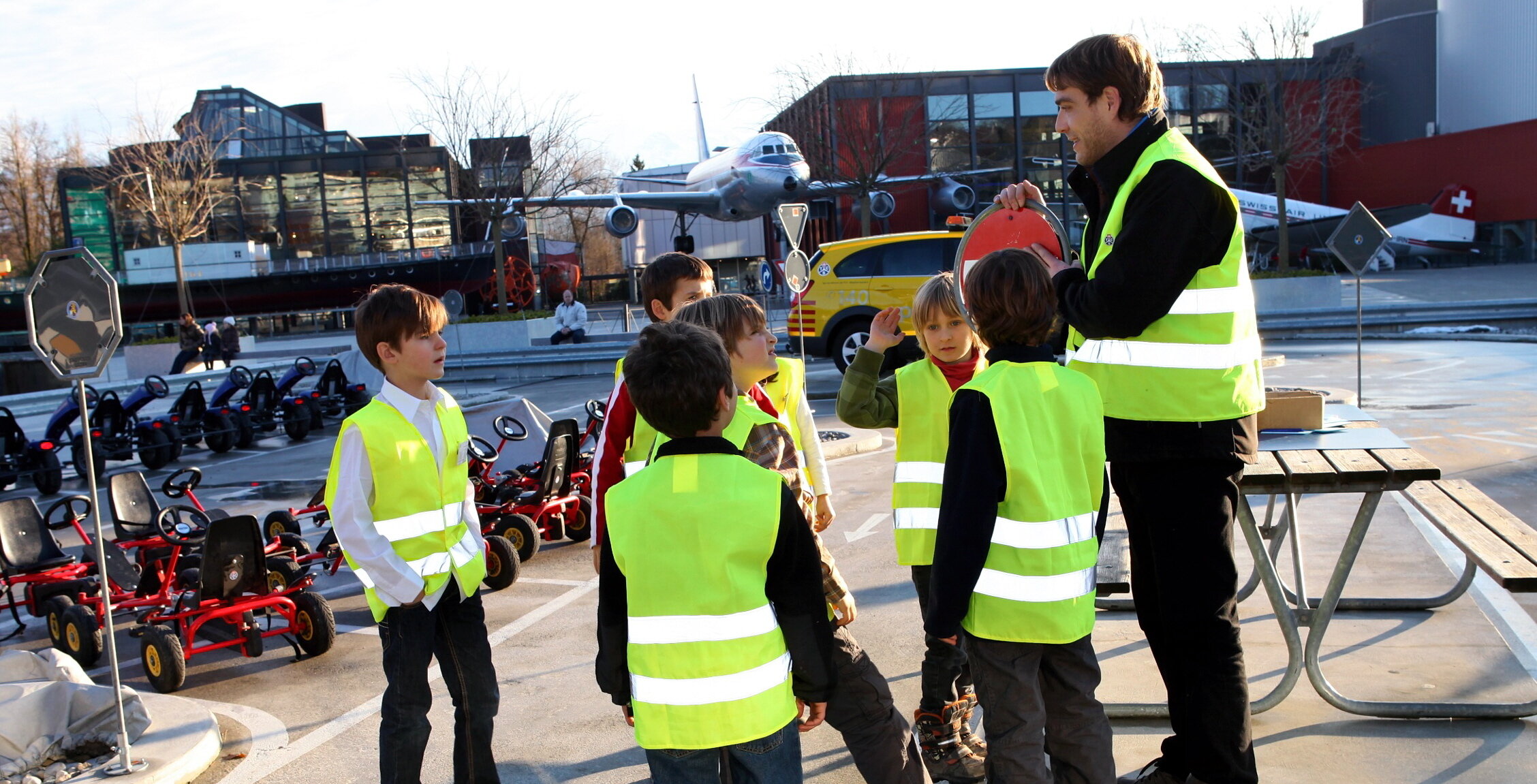 Fünf Kinder mit Leuchtwesten und eine Begleitperson mit Leuchtweste, sie stehen im Verkehrsgarten im Verkehrshaus.