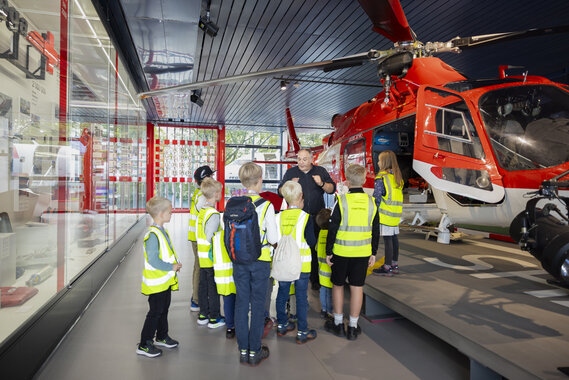 Fünf Kinder mit Leuchtwesten und eine Begleitperson mit Leuchtweste, sie stehen im Verkehrsgarten im Verkehrshaus.