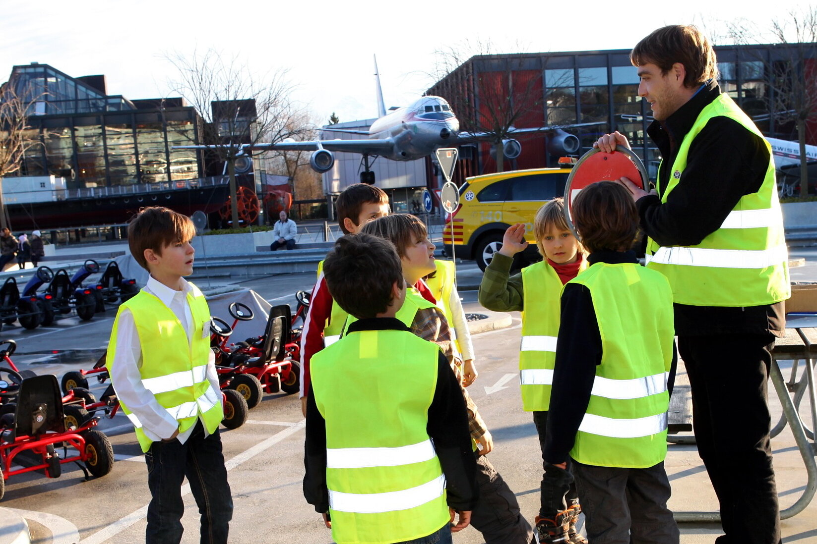 Fünf Kinder mit Leuchtwesten und eine Begleitperson mit Leuchtweste, sie stehen im Verkehrsgarten im Verkehrshaus.