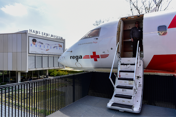 Ein Schweizer Ambulanzflugzeug ist an das Hans Erni Museum angedockt, ein Mann steht an der offenen Tür und eine Treppe führt nach unten.