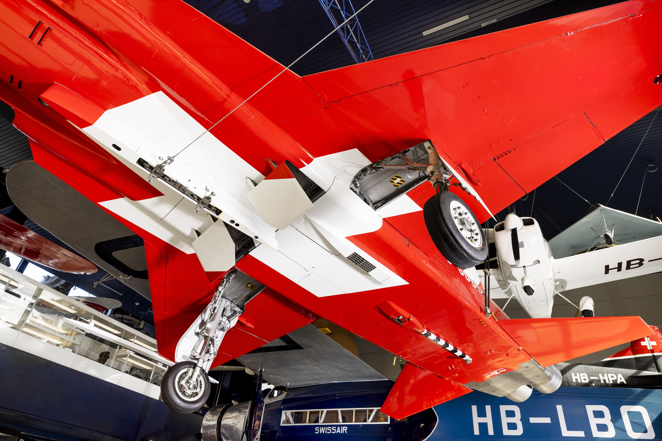 Ein rotes Flugzeug mit einem weissen Kreuz, fotografiert von unten.