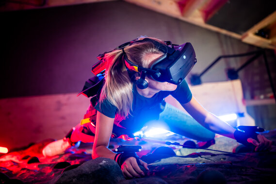 Eine rau klettert mit einer VR-Brille eine Kletterwand hoch.