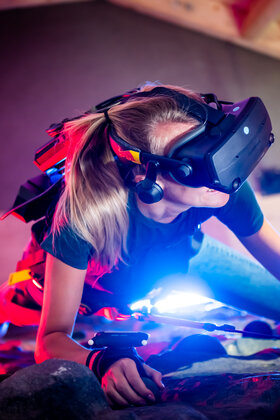 Eine rau klettert mit einer VR-Brille eine Kletterwand hoch.