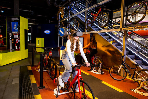 Ein junges Mädchen auf einem stationären Fahrrad trägt ein VR-Headset.