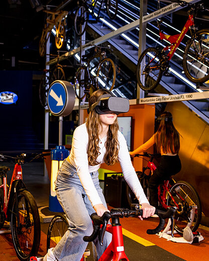 Ein junges Mädchen auf einem stationären Fahrrad trägt ein VR-Headset.