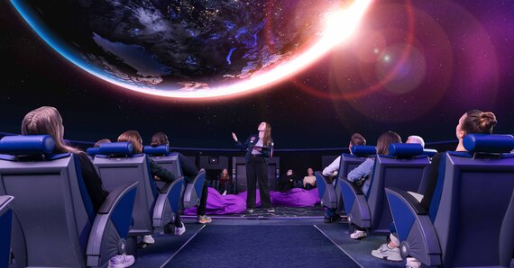 Eine Gruppe von Menschen sitzt in einem Planetarium und blickt auf eine lebendige Projektion der Erde und des Kosmos darüber.