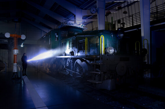 Eine Person mit Taschenlampe zündet im Dunkeln auf die Eisenbahn Krokodil.