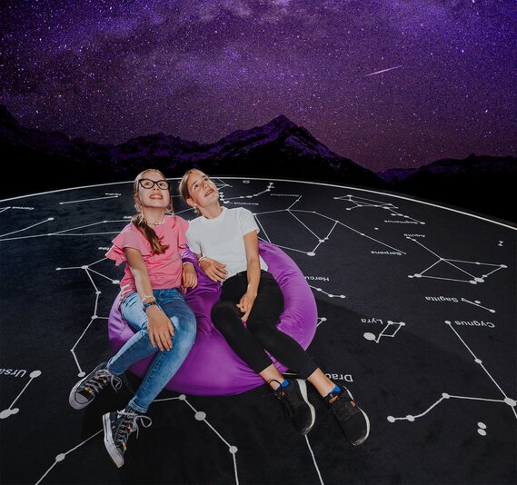 Zwei Mädchen in einem Sitzsack blicken im Planetarium im Verkehrshaus in den Sternenhimmel. 