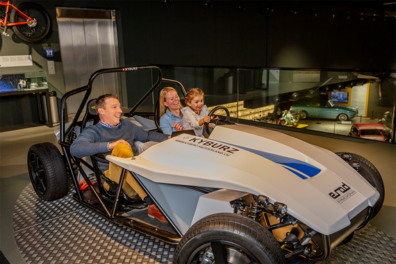 Eine Familie geniesst eine Fahrt in einem Elektrofahrzeug in einem Museum, das eine Mischung aus modernem Design und interaktivem Erlebnis bietet.