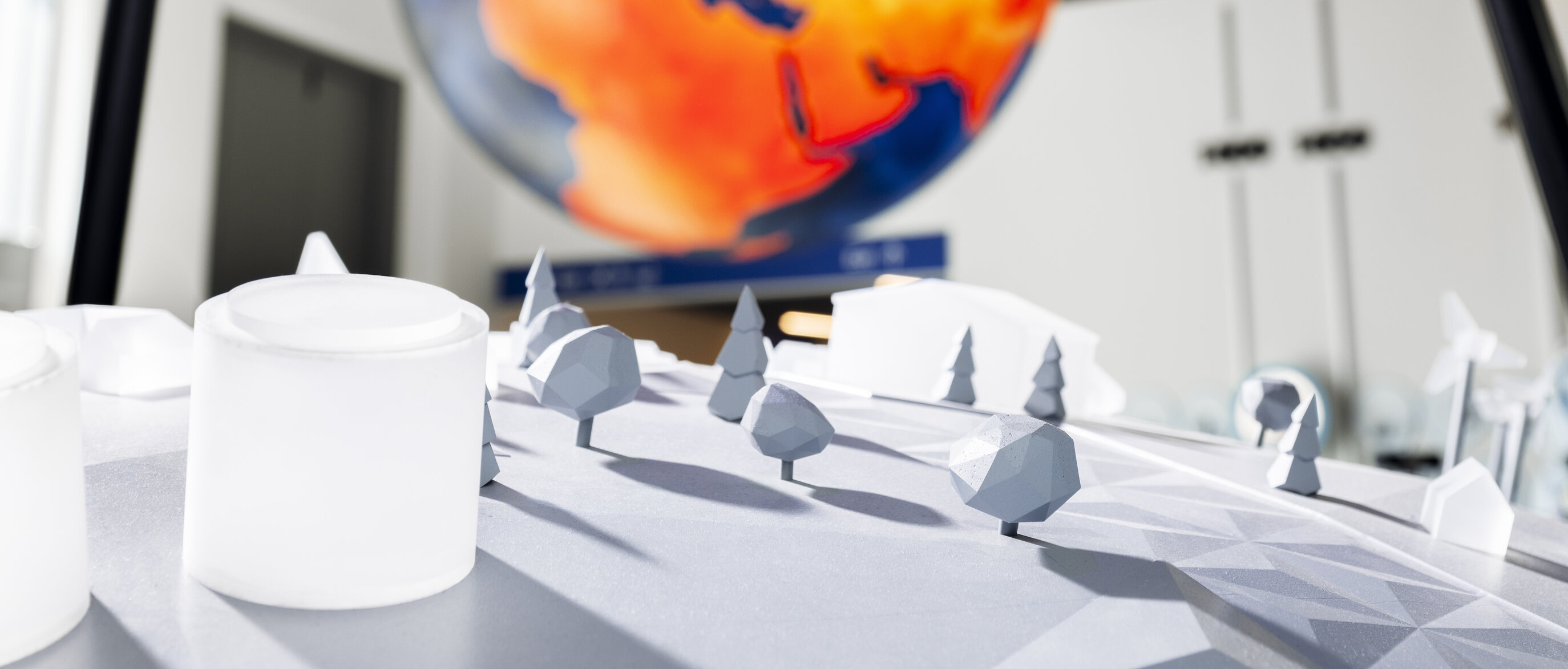 Von der Decke hängt ein großer Globus, der die thermische Signatur anzeigt. Im Vordergrund ist in weiss eine Miniaturlandschaft zu sehen.