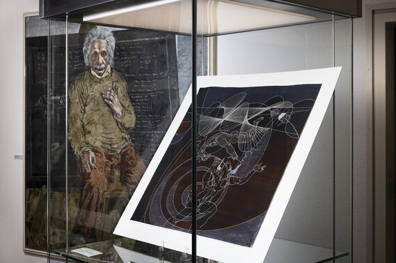 Ein Bild von Einstein und davor ein Bild von Hans Erni in einem Glaskasten.