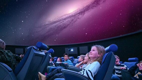 Ein 10 jähriges Mädchen schaut begeistert in den Himmel des Planetariums in Luzern. 