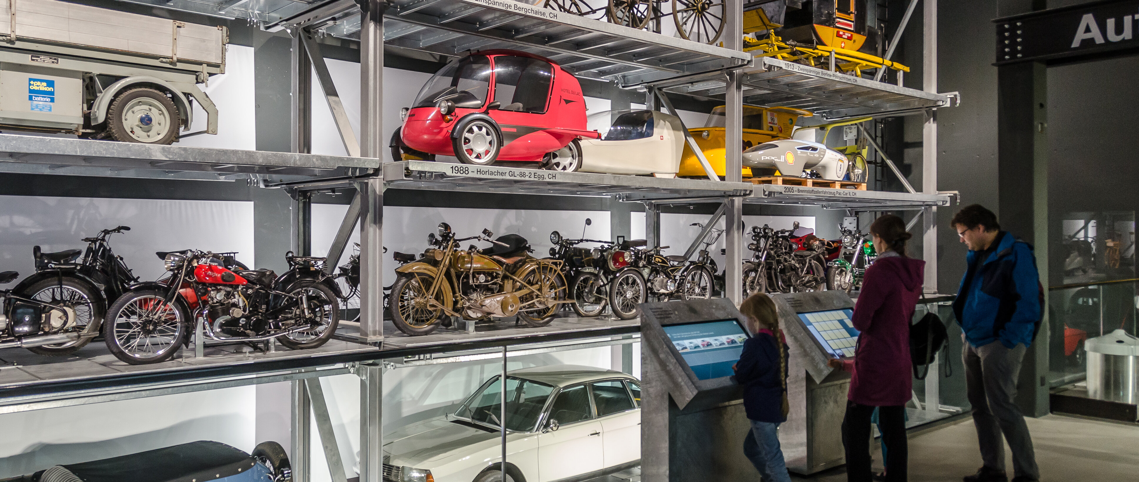 Eine dreiköpfige Familie steht vor dem Schaulager in der Autohalle im Verkehrshaus. 